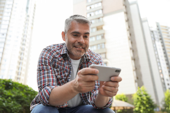 Portrait of handsome mature man using mobile phone in city center
