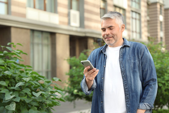 Portrait of handsome mature man using mobile phone in city. Space for text