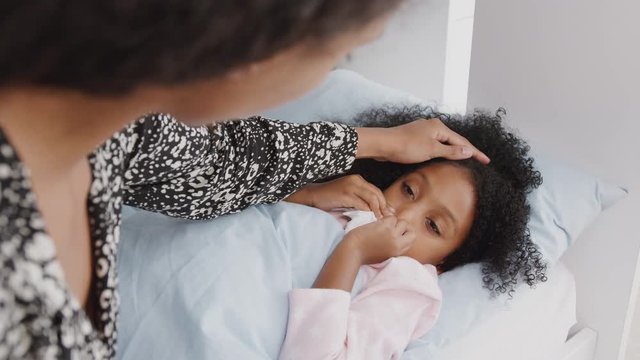 Mother Caring For Sick Daughter Ill In Bed With Cold Handing Her A Tissue