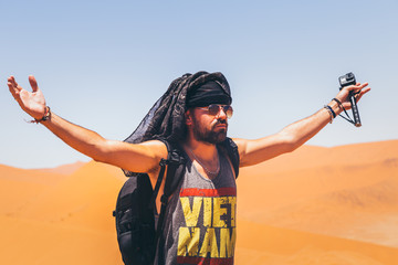 Homme les bras en l'air dans le désert avec foulard et lunettes de soleil