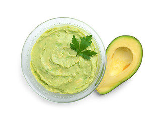 Glass bowl of tasty guacamole with parsley and cut avocado on white background, top view