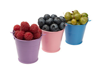 Berries of ripe raspberry, blueberry (blueberry), gooseberry in full lilac and pink and blue buckets. On white background, isolated. Close-up. Still life.