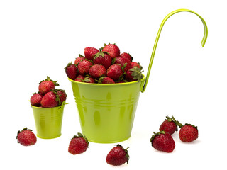 Ripe strawberries in large and small green buckets. And also scattered around. On white background, isolated. Still life. Close-up.
