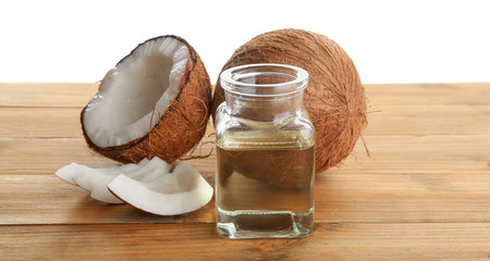 Ripe coconuts and jar with natural organic oil on wooden table against white background