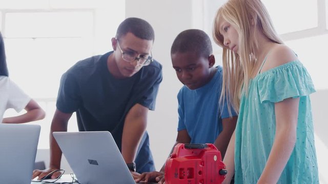 Students With Male Teacher In After School Computer Coding Class Learning To Program Robot Vehicle