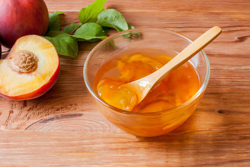 Piala with a spoon in homemade peach jam on a wooden round stand on the table in the morning sun. The concept of homemade conservation. Close up