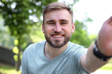 Naklejka na ściany i meble Happy young man taking selfie in park