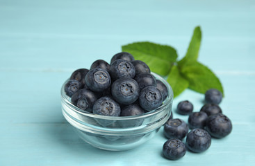 Glass bowl of tasty blueberries on color wooden table