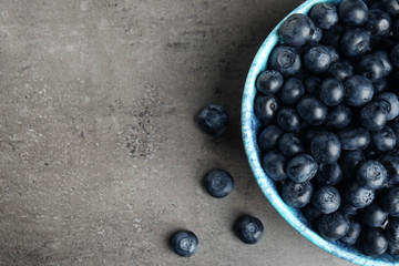 Bowl of tasty blueberries on grey table, top view with space for text