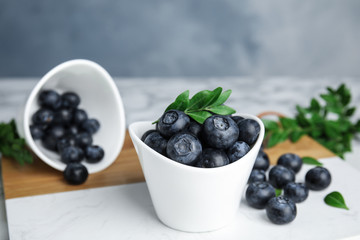 Bowls with tasty fresh blueberries and leaves on table