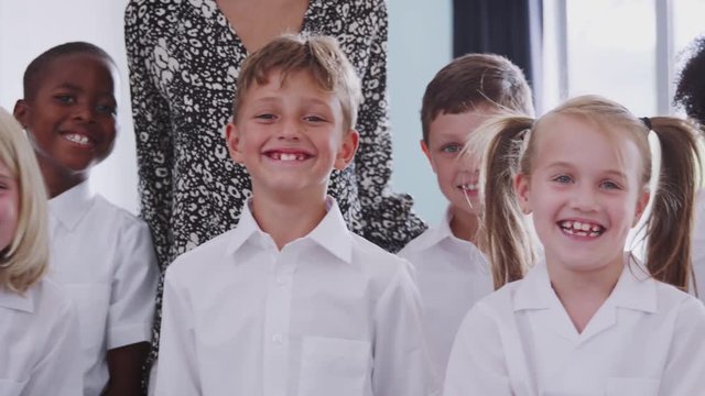 Portrait Of Elementary School Pupils Wearing Uniform In Classroom With Male Teacher