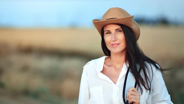 Beautiful backpacker female in hat posing at wheat field background looking at camera