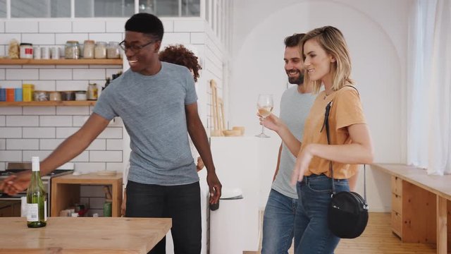 Couple Greeting Friends Arriving For Dinner Party At Home With Wine