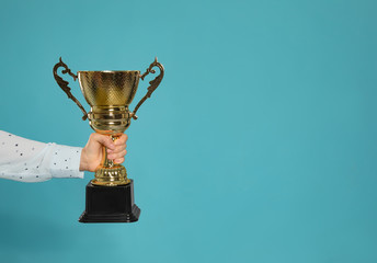 Young woman holding gold trophy cup on blue background, closeup with space for text