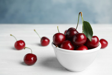 Bowl with sweet cherries on white wooden table. Space for text