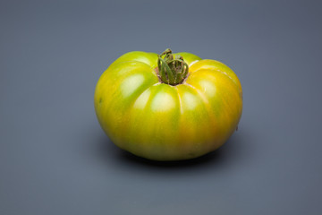 Tomate verde sobre fondo liso, tomate ecológico recién cogido del huerto.