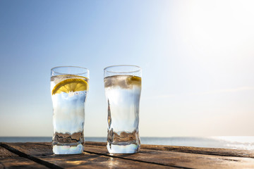 Wooden table with glasses of refreshing lemon drink on hot summer day outdoors, space for text