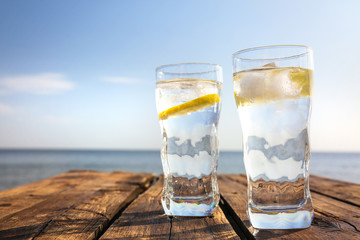 Wooden table with glasses of refreshing lemon drink on hot summer day outdoors, space for text