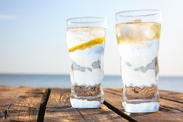 Wooden table with glasses of refreshing lemon drink on hot summer day outdoors, space for text