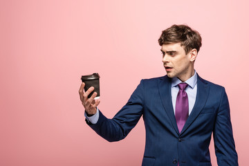 surprised businessman looking at disposable cup on pink background