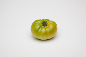 Tomate verde sobre fondo liso, tomate ecológico recién cogido de la mata, tomate verde para que madure fuera de la planta