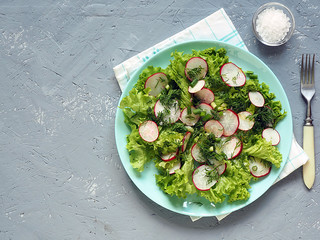 Salad of radish and greens on a plate, on a gray concrete background.