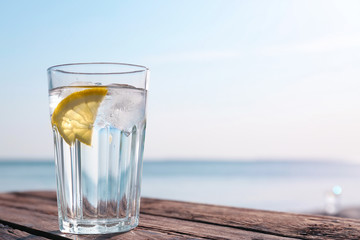 Wooden table with glass of refreshing lemon drink on hot summer day outdoors, space for text