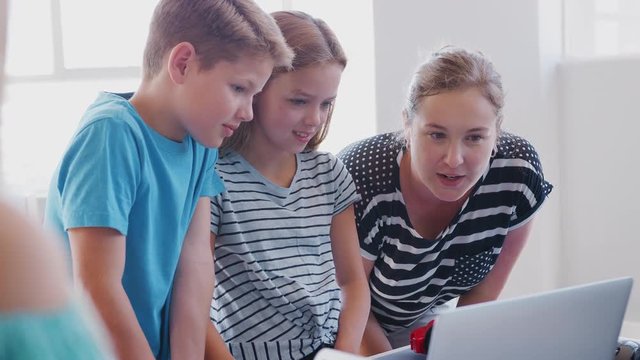 Two Students With Female Teacher In After School Computer Coding Class Learning To Program Robot Vehicle
