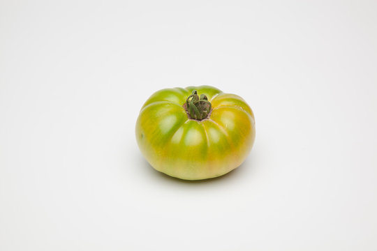 Tomate verde sobre fondo liso, tomate ecol&oacute;gico reci&eacute;n cogido de la mata, tomate verde para que madure fuera de la planta