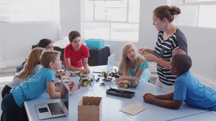 Students With Female Teacher In After School Computer Coding Class Learning To Program Robot Vehicle