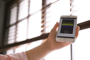 Woman using smart home application on phone to control window blinds indoors, closeup