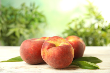 Fototapeta na wymiar Fresh peaches and leaves on white wooden table against green blurred background