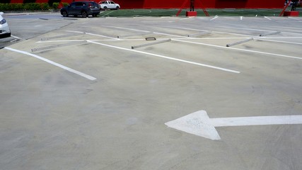 Traffic arrow sign with white lines and concrete wheel stoppers in parking lot or outdoor car park area, selective focus