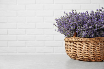 Fresh lavender flowers in basket on stone table against white brick wall, space for text