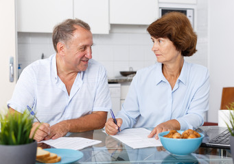 Fototapeta na wymiar Smiling mature couple at table filling up documents at table in home
