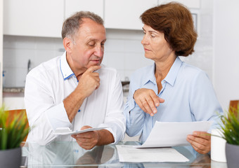 Obraz premium Sad mature couple at kitchen table sitting with financial documents