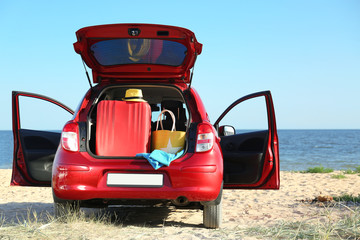Suitcase and beach accessories in car trunk on sand near sea. Space for text