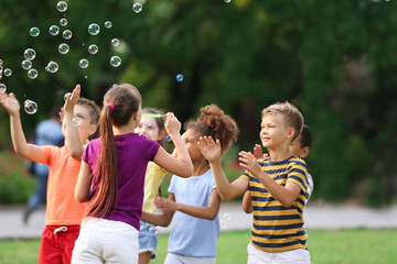 Cute little children playing with soap bubbles in park