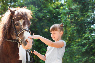 Cute little girl with her pony in green park