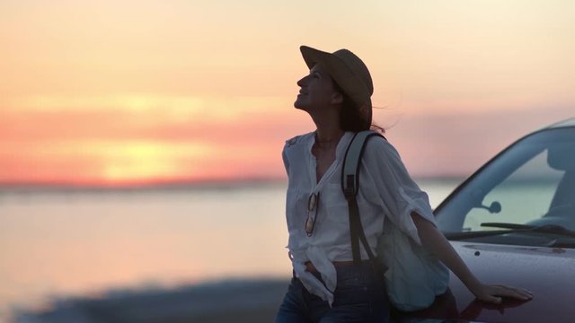 Relaxed backpacker smiling woman enjoying natural seascape at sunset during car travel medium shot