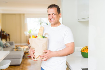 Middle age man holding grocieries bag full of vegetables at home
