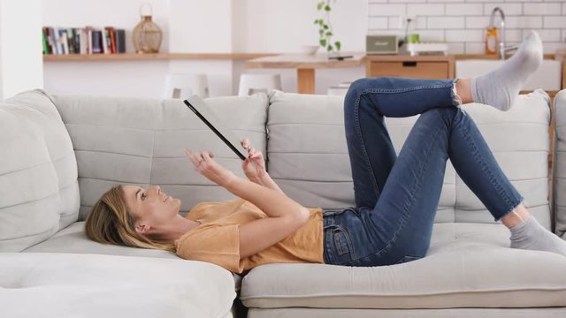Woman Relaxing Lying On Sofa At Home Looking At Digital Tablet