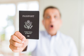 Middle age man holding holding passport of United States scared in shock with a surprise face, afraid and excited with fear expression