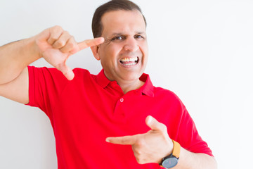 Middle age man wearing red t-shirt over white wall smiling making frame with hands and fingers with happy face. Creativity and photography concept.