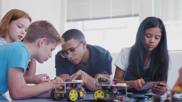 Students With Male Teacher In After School Computer Coding Class Learning To Program Robot Vehicle
