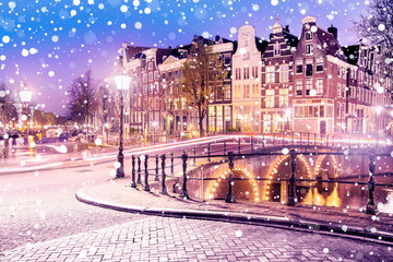 Traditional Dutch old houses and bridges on the canals in Amsterdam on a snowy winter night, The...