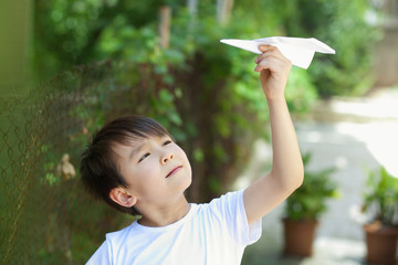 Happy cute Asian child boy playing with paper airplane outdoors