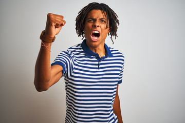 Afro man with dreadlocks wearing striped blue polo standing over isolated white background angry and mad raising fist frustrated and furious while shouting with anger. Rage and aggressive concept.