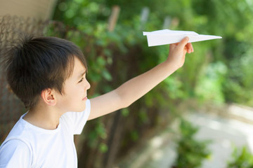 Happy cute Asian child boy playing with paper airplane outdoors