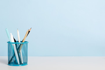Blue, white and black pencils, pens in a stand on a white table on a blue background, office desk....